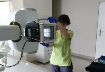 Zdjęcie przedstawia słuchacza wykonującego badanie diagnostyczne z zakresu elektrokardiologii. Widzimy aparat rentgenowski i dotykającego go słuchacza