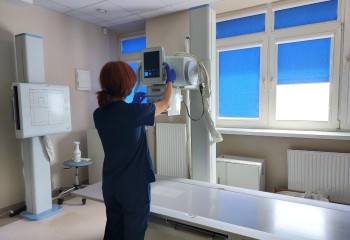 Zdjęcie przedstawia słuchacza wykonującego badanie diagnostyczne z zakresu elektrokardiologii. Widzimy aparat rentgenowski i dotykającego go słuchacza